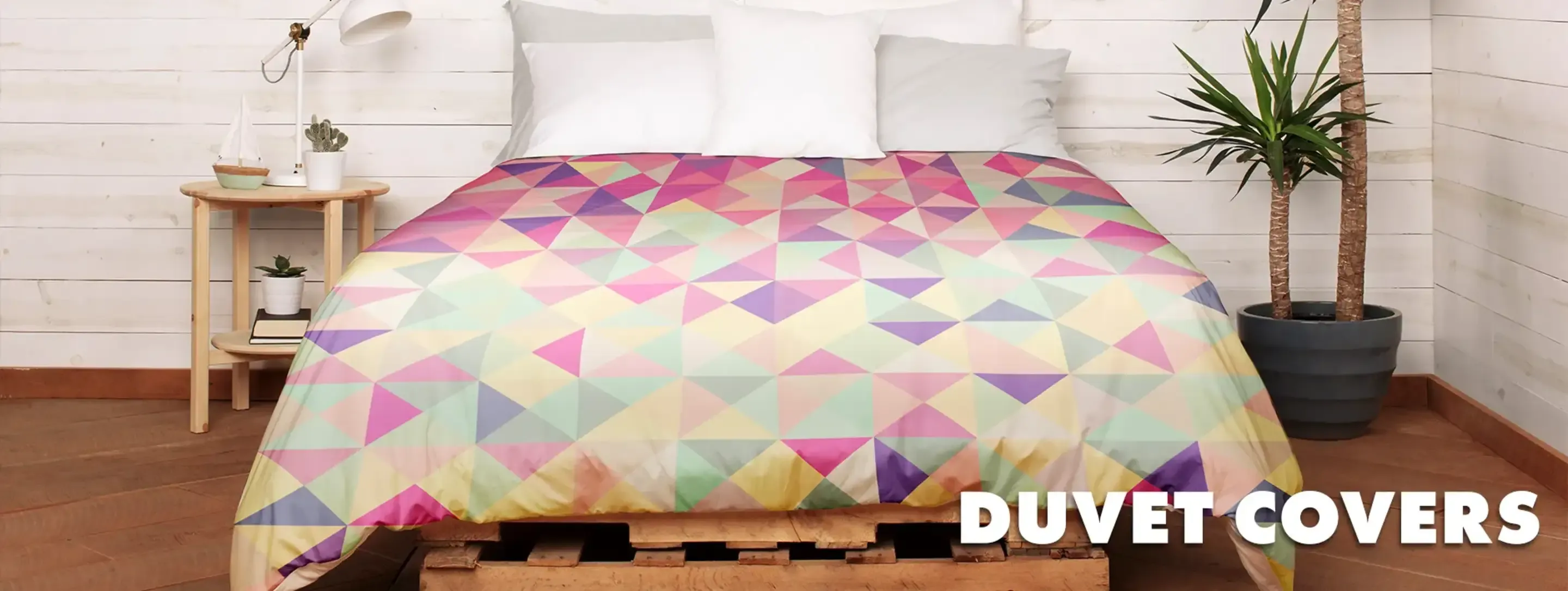 Pink and yellow triangle pattern duvet cover on bed in white bedroom with plants and 'Duvet Covers' text.