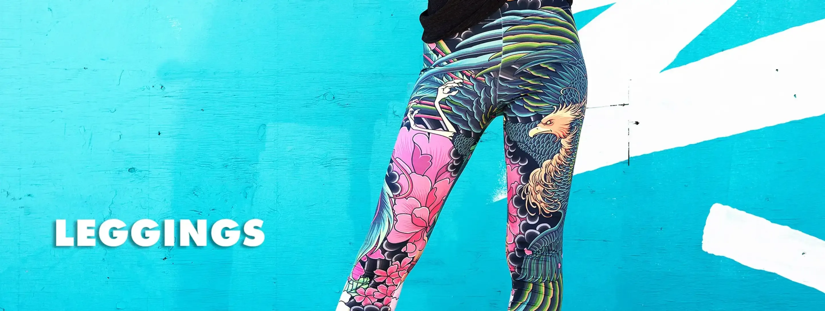 Woman's legs in colorful phoenix print women's leggings against teal painted wall with white street art.