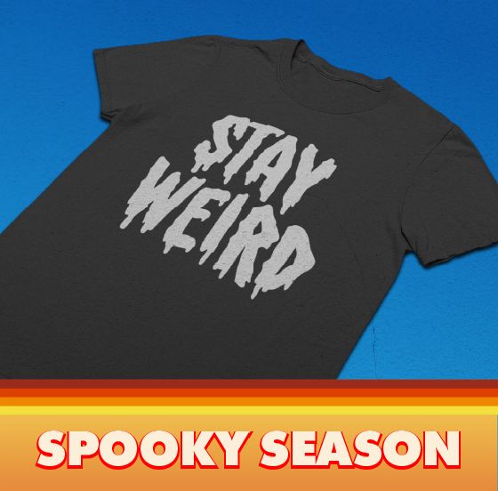Black t-shirt with Deniart's dripping Stay Weird graphic laid flat on a bright blue background