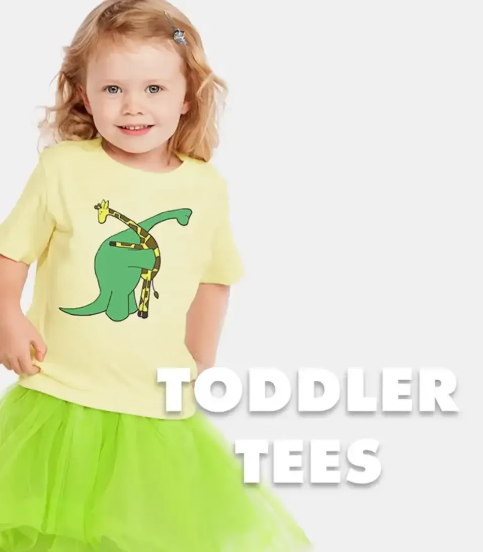 Smiling toddler in yellow t-shirt with dinosaur graphic and green tutu skirt labelled 'Toddler Tees'.