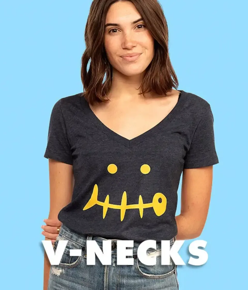 Woman in dark gray women's v-neck t-shirt with yellow fish skeleton smiley graphic on light blue backdrop.