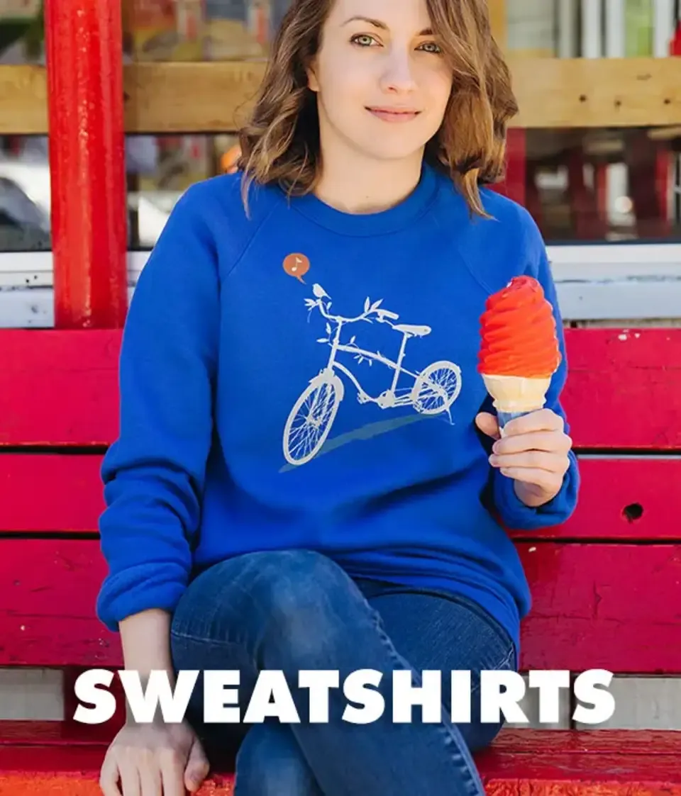 Woman in blue women's sweatshirt with white bicycle graphic, holding ice cream cone on red bench outdoors.