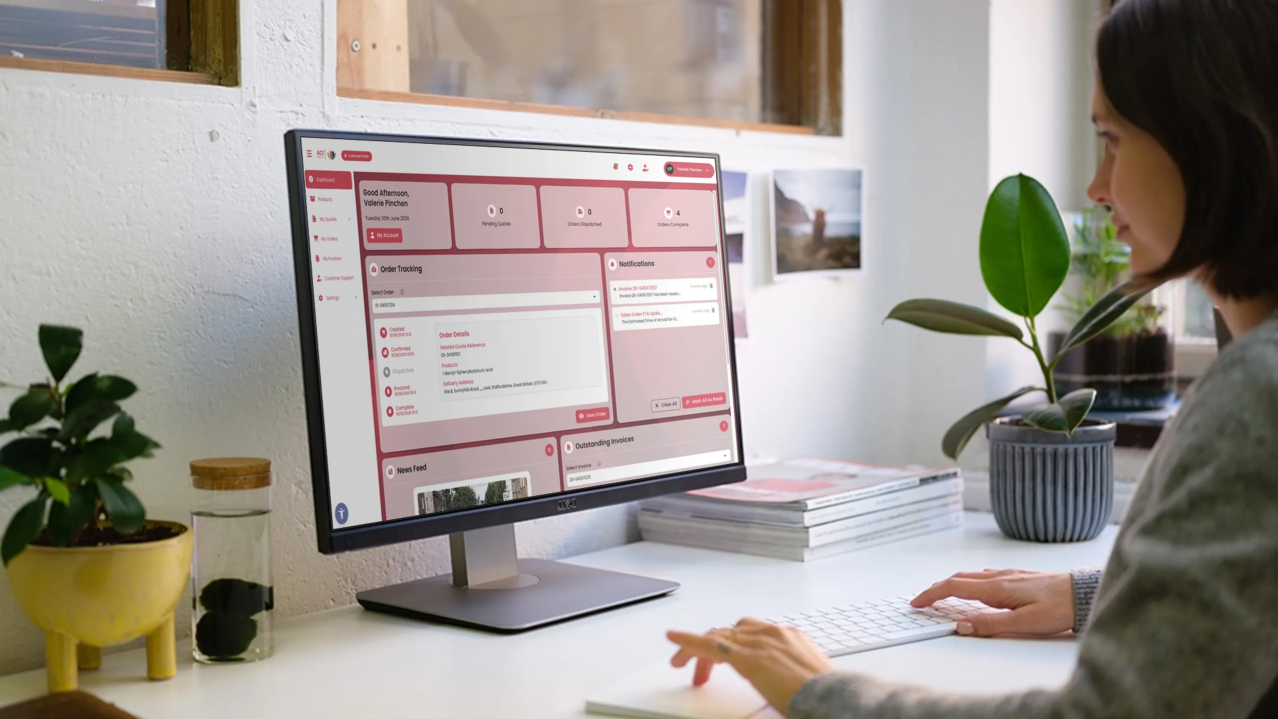 Woman using a desktop computer in a office, interacting with a customer portal surrounded by potted plants and books.