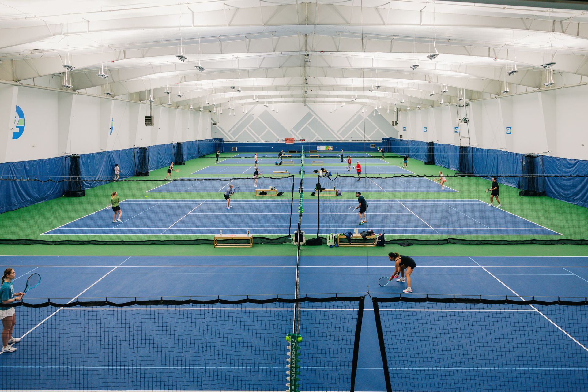 Galbraith Indoor tennis center with multiple blue courts, players actively engaged in matches, and blue curtains lining the walls.