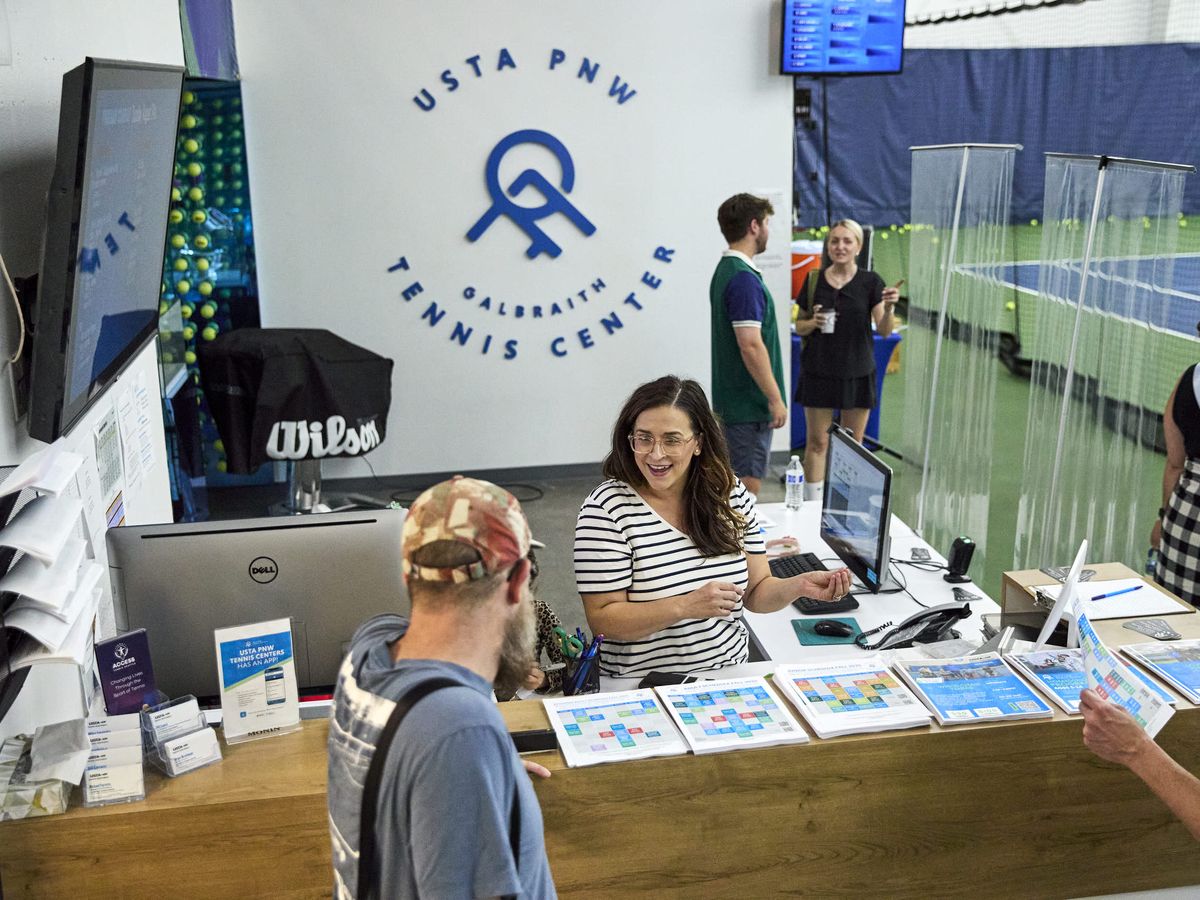 Reception area at USTA PNW Galbraith Tennis Center with staff assisting visitors, tennis courts visible in the background.