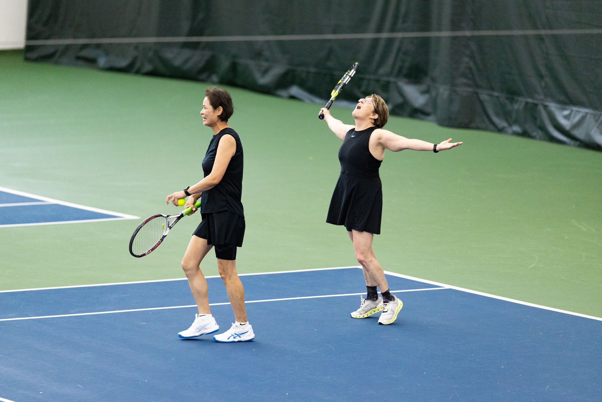 Two people playing tennis on an indoor court; celebrating a win at Adult 55 Section Championships.