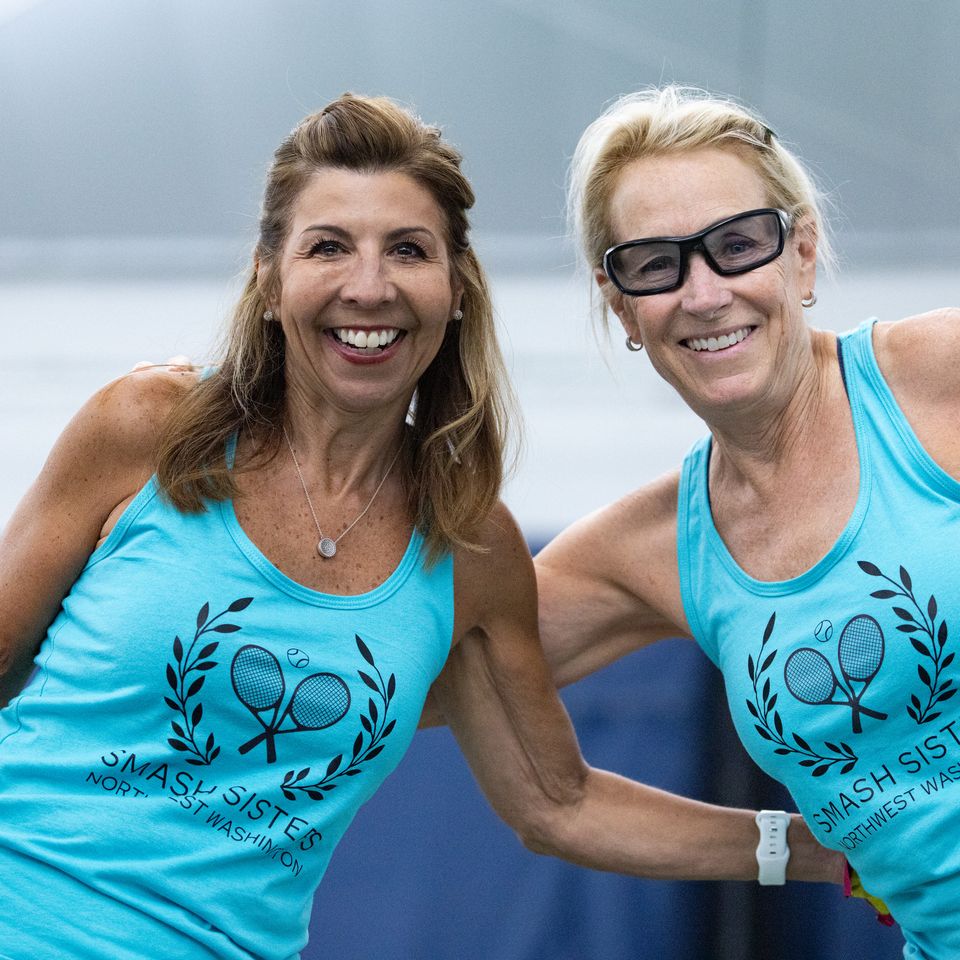 Two smiling women in matching turquoise tank tops with "Smash Sisters" logo, posing side by side on a tennis court.