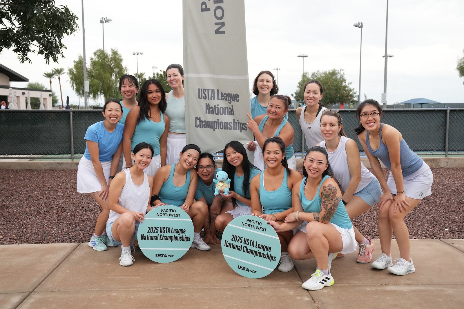 A women's tennis team poses with circular plaques, celebrating their achievement at the 2023 USTA League National Championships.