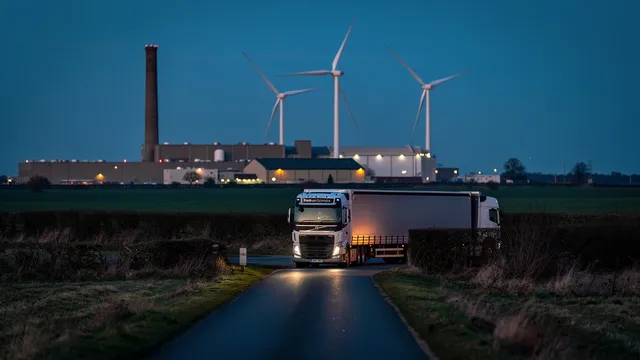A UK paper mill at dusk with wind turbines turning behind it and a haulage lorry leaving on a country lane in Lincolnshire