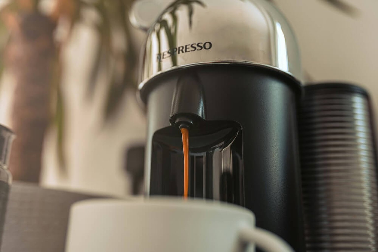 A hand uses a wooden-handled tamper on coffee grounds in a portafilter on a wooden countertop.
