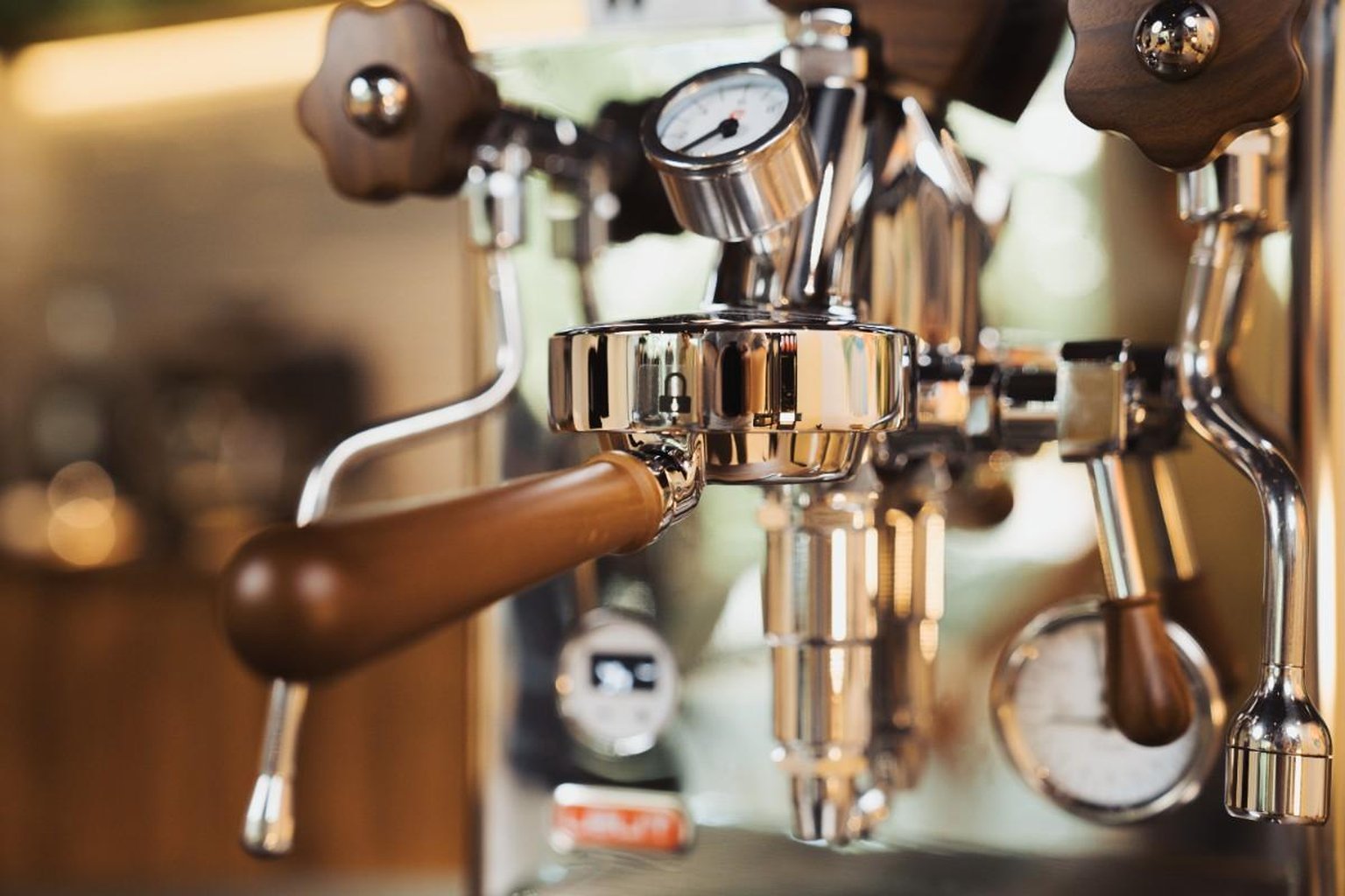 Close-up of a polished espresso machine with steam wand and pressure gauge, featuring wood accents and a shiny metallic finish.