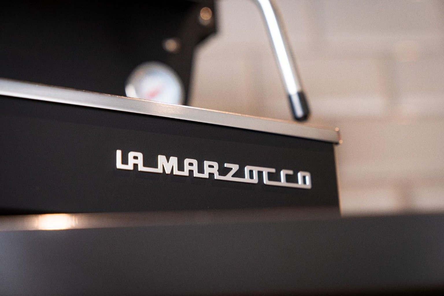 Close-up of a La Marzocco espresso machine with sleek metal details and a visible gauge, set against a blurred background.