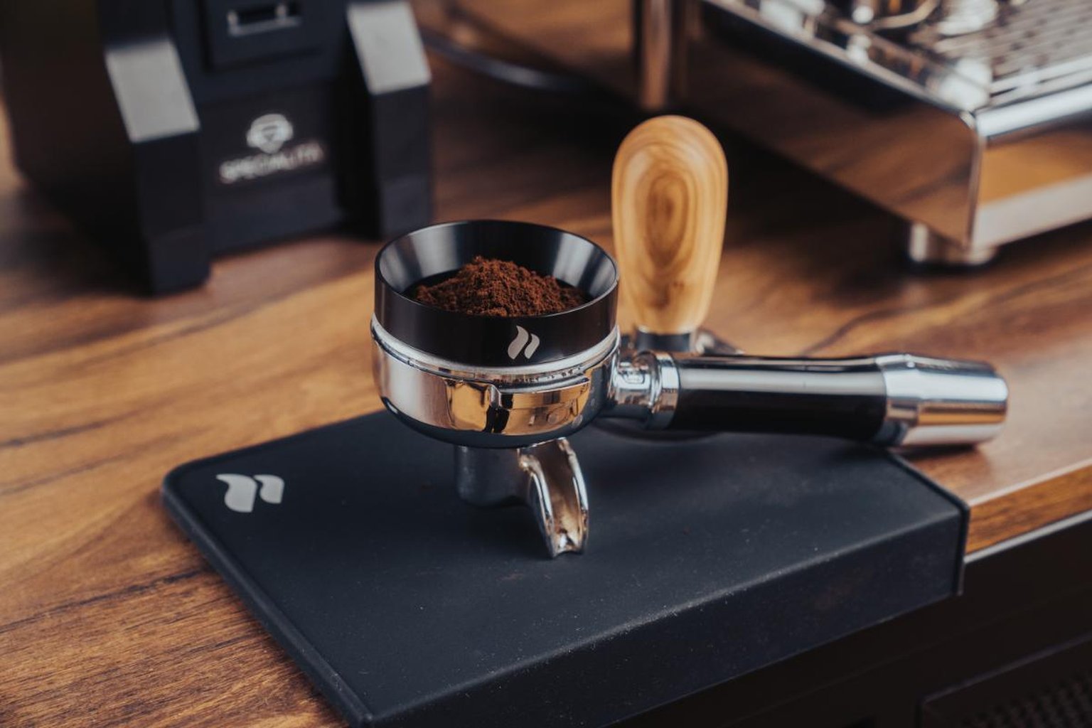 a wooden-handled tamper on coffee grounds in a portafilter on a wooden countertop.