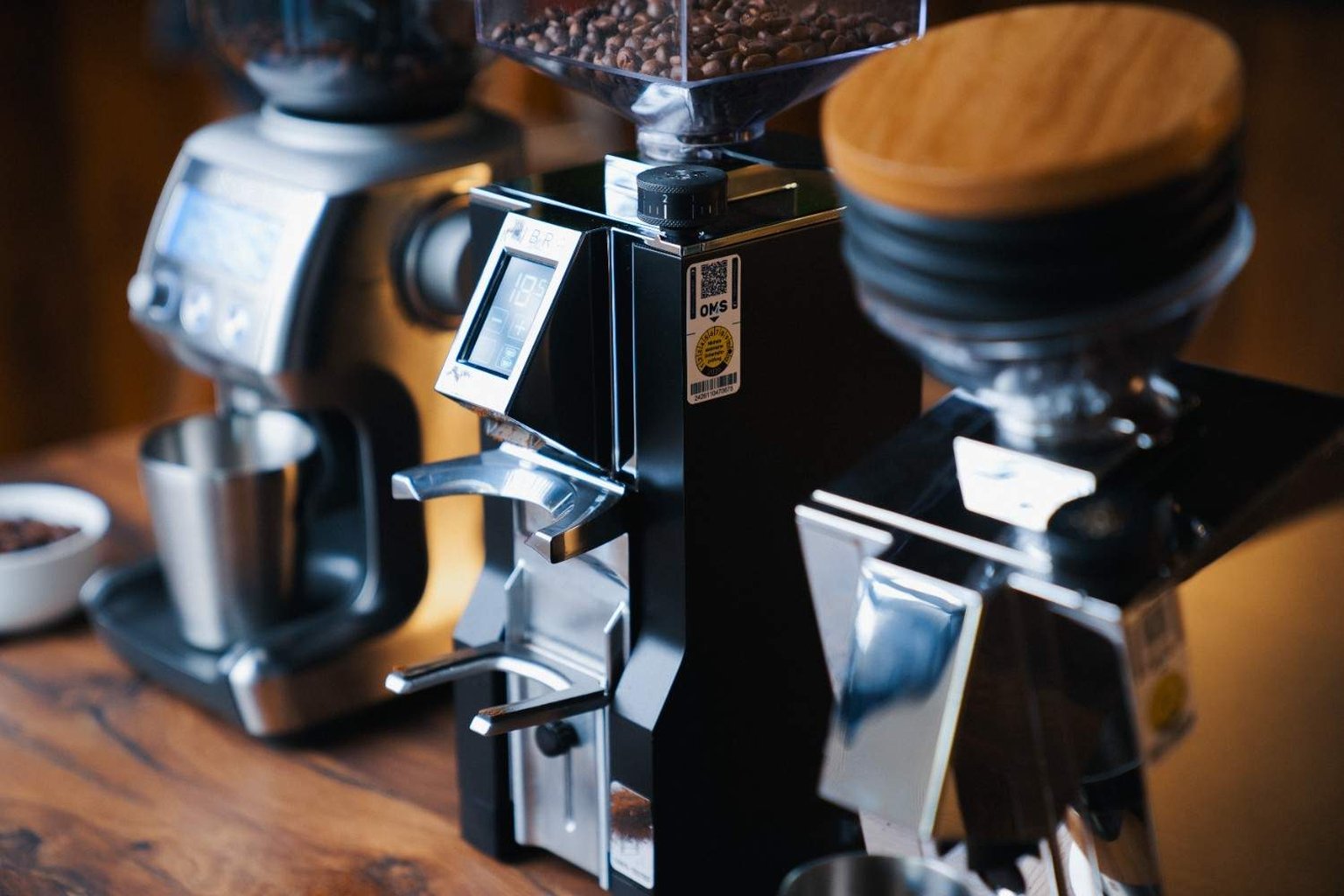 Modern coffee grinders on a wooden counter, featuring digital displays and containers filled with coffee beans.