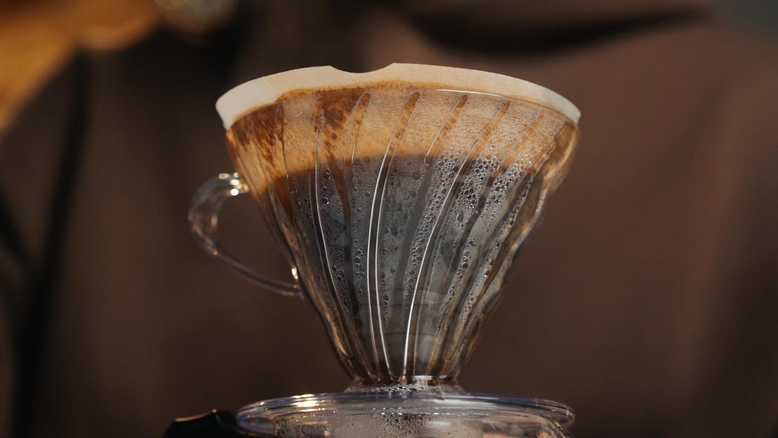 Una mano usa un tamper de mango de madera sobre café molido en un portafiltro, encima de una encimera de madera.