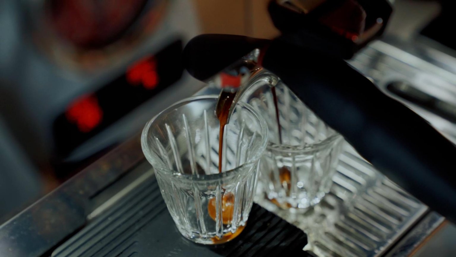 coffee dripping out of a espresso machine into espresso cups