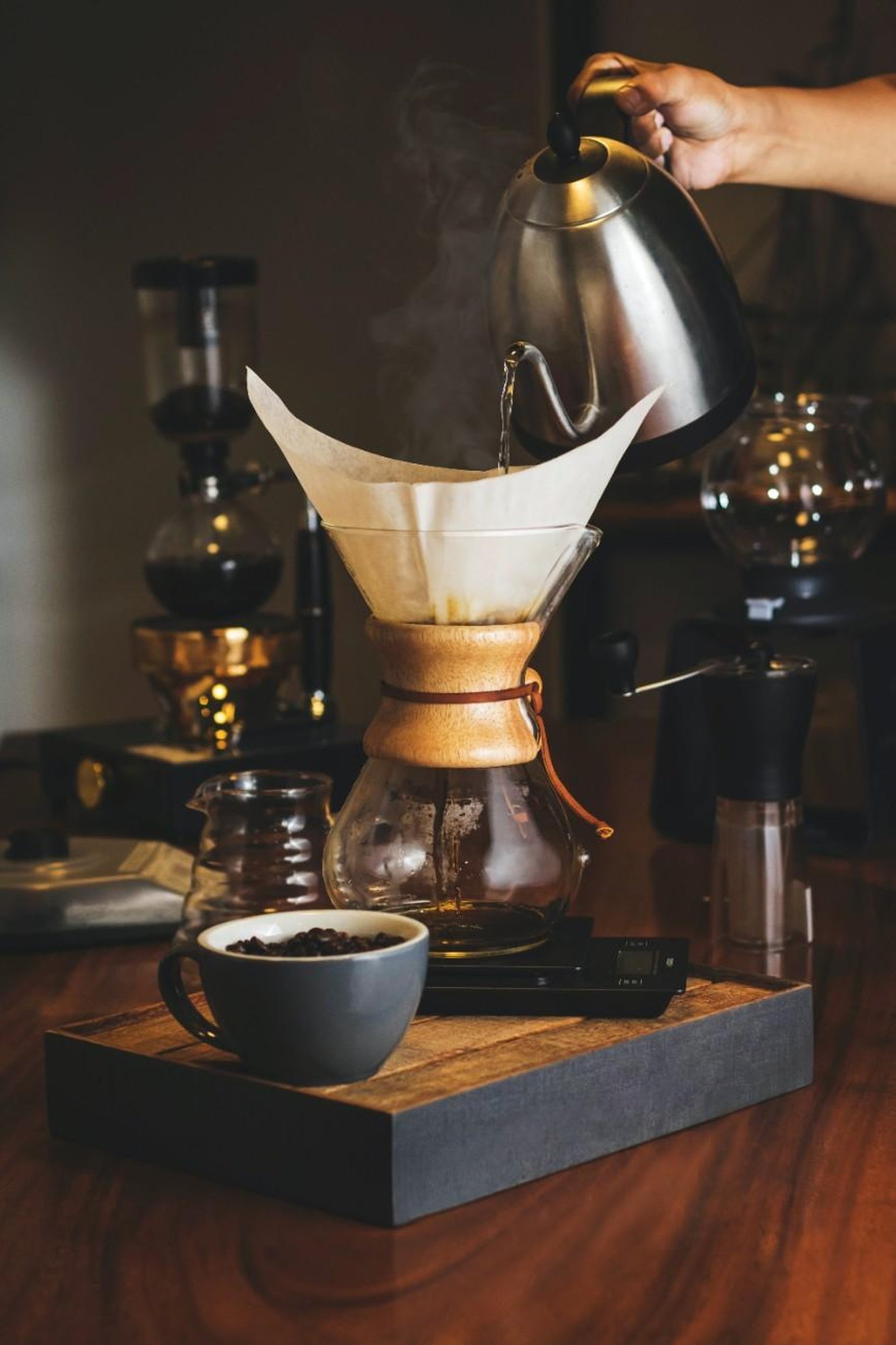 A Chemex coffee maker on a wooden surface with a glass of freshly brewed pour over coffee.