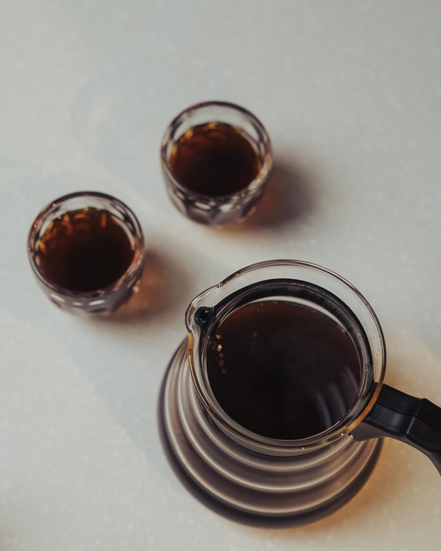 A hand uses a wooden-handled tamper on coffee grounds in a portafilter on a wooden countertop.
