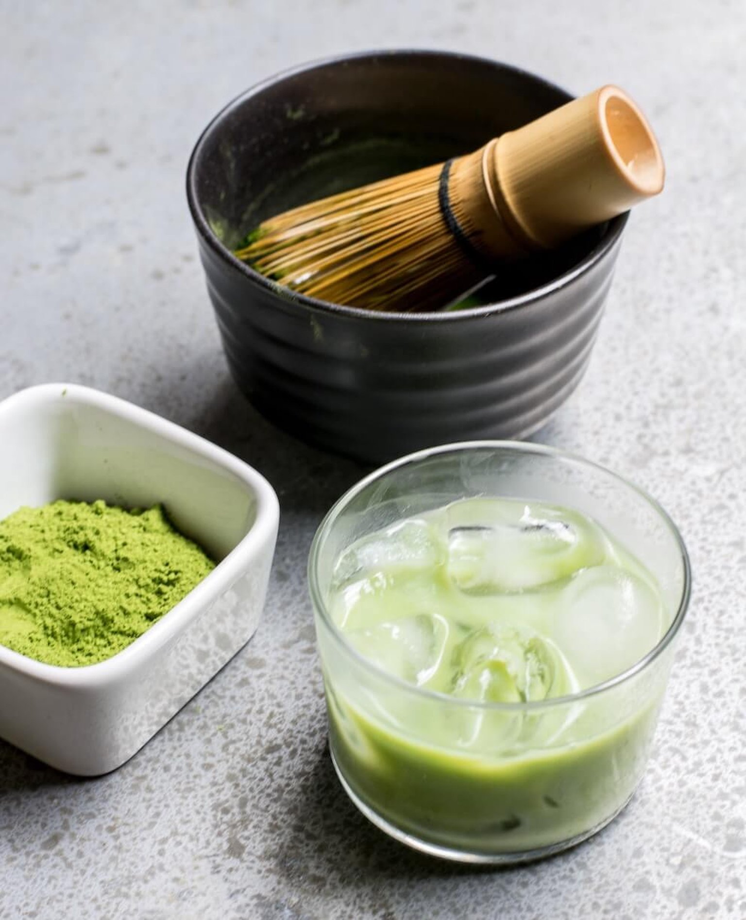 A bowl of vibrant green matcha powder with a bamboo whisk on a wooden surface.