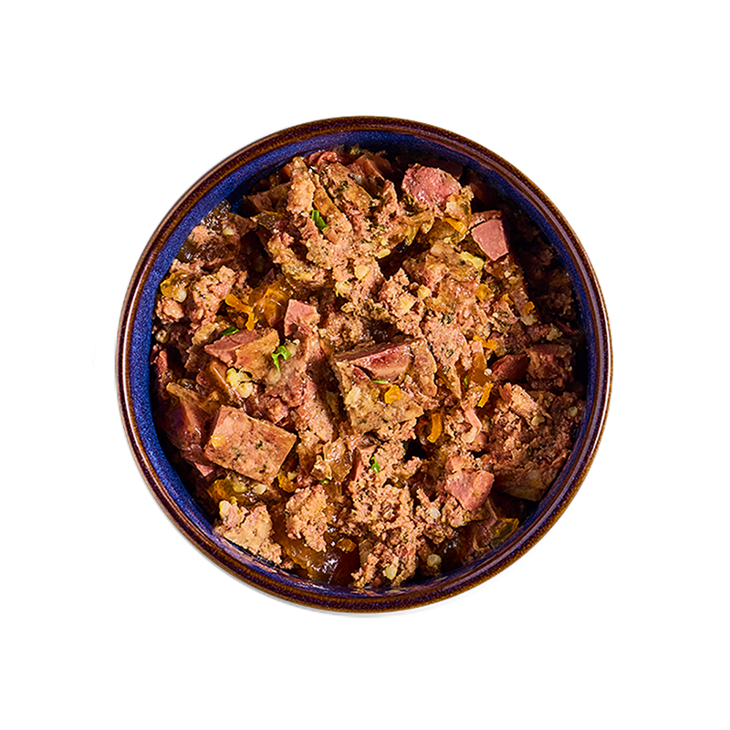 A bowl filled with chunky Tails.com wet food, featuring pieces of meat and vegetables in a brown sauce and bits of vegetables.