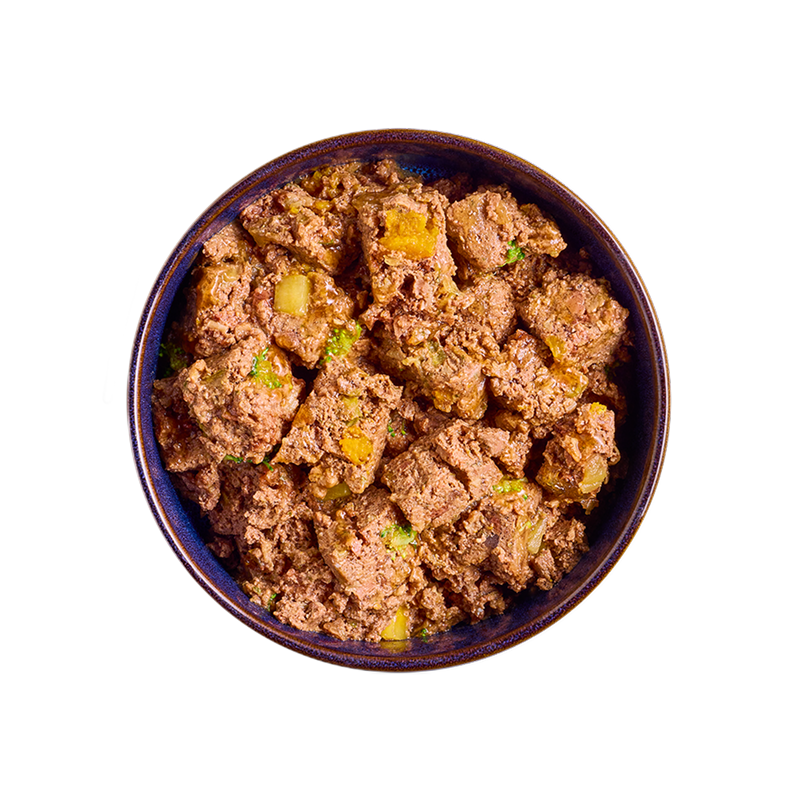 A bowl filled with chunky Tails.com wet food, featuring pieces of meat and vegetables in a brown sauce and bits of vegetables.