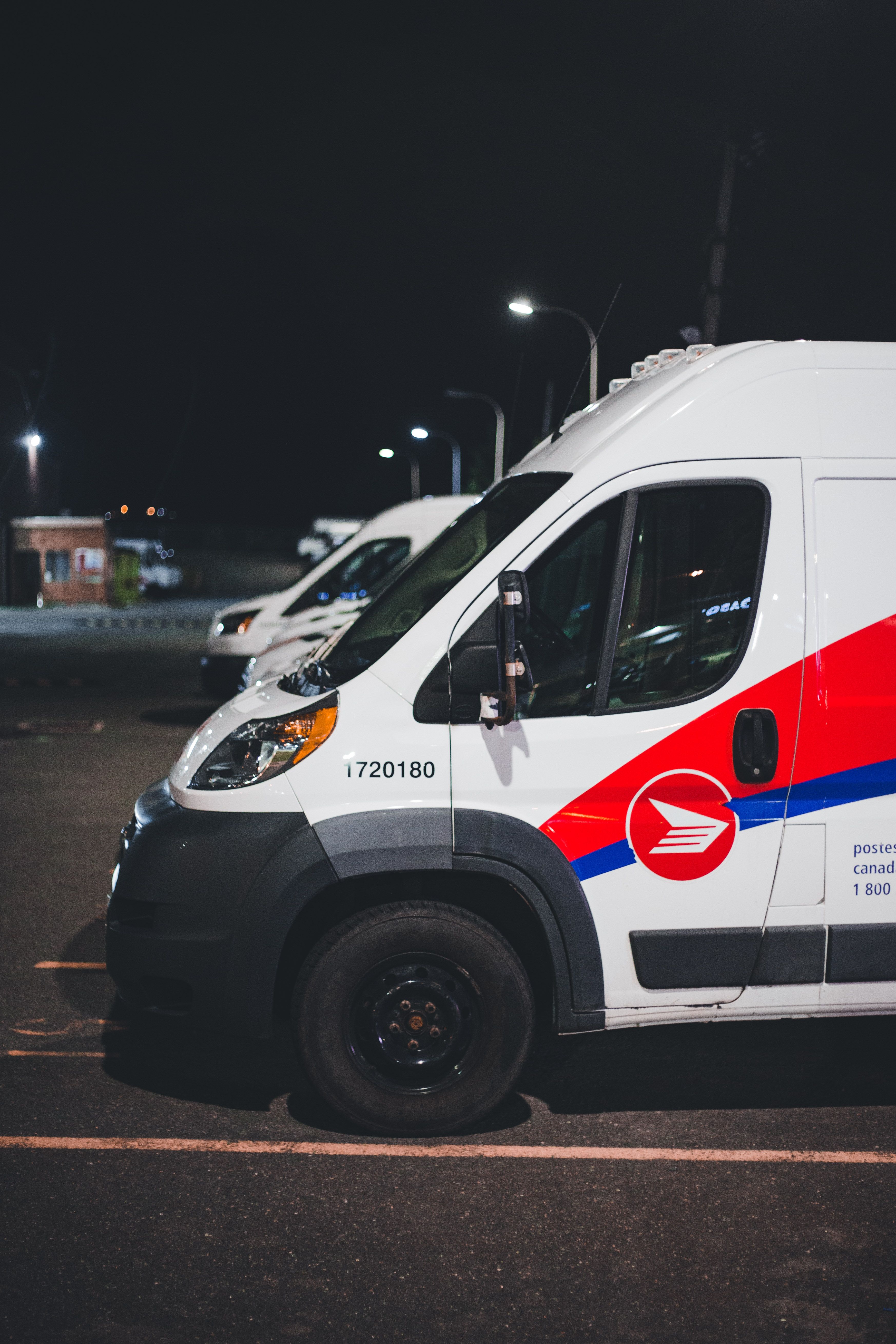 Postal service van parked at night, displaying a red and blue logo on its side, with another van visible in the background.