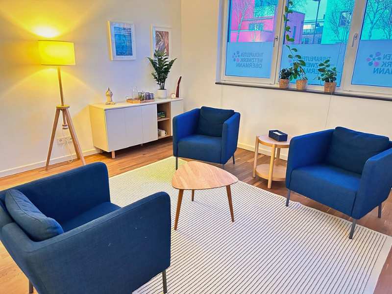 Heller Therapieraum der Praxis in Lübeck mit drei dunkelblauen Sesseln und Holztisch