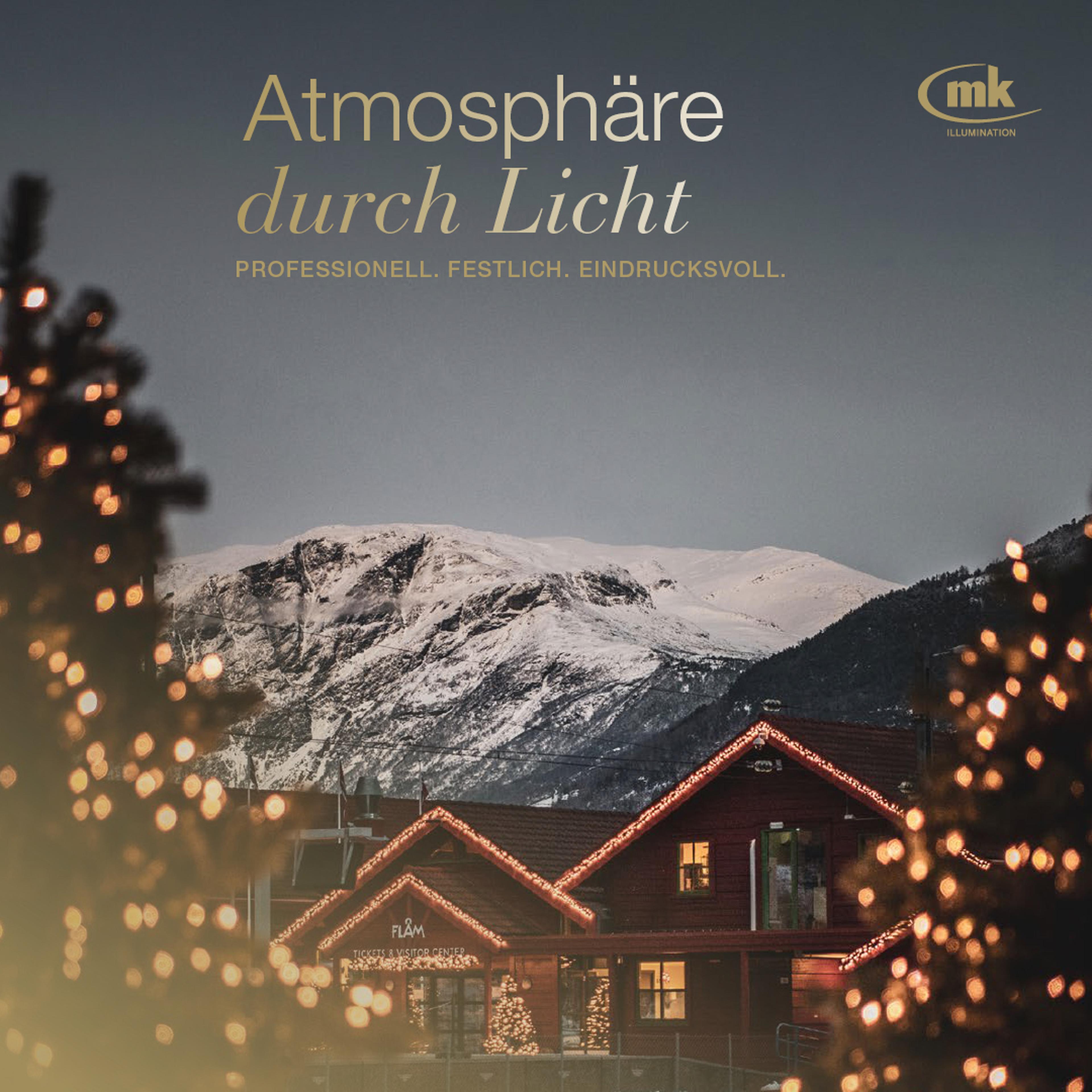 Beleuchtetes Gebäude vor schneebedeckten Bergen, umgeben von dekorativen Lichtern und Tannen.
