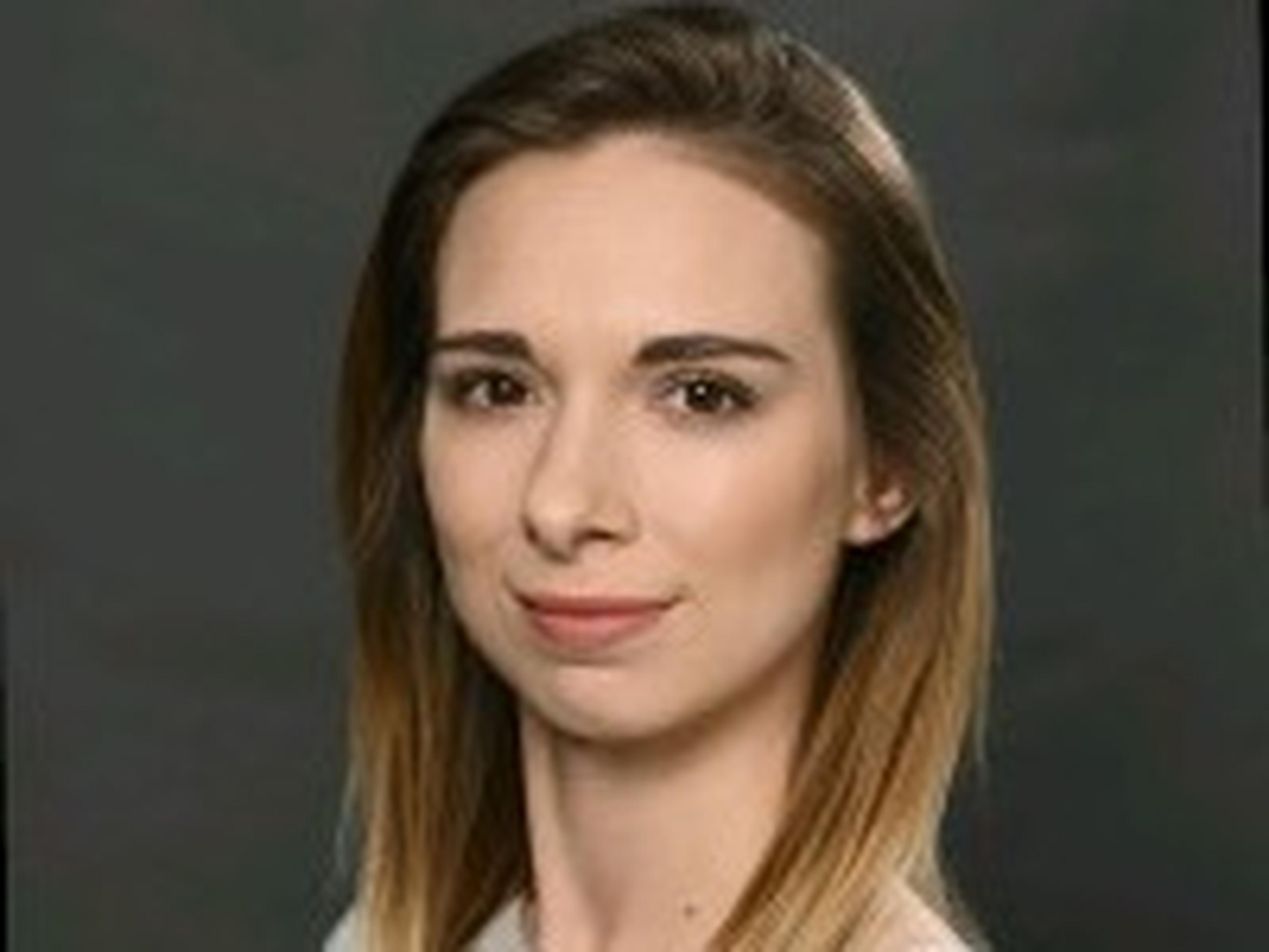 Portrait of a person with shoulder-length ombre hair, wearing a white top, against a dark background.