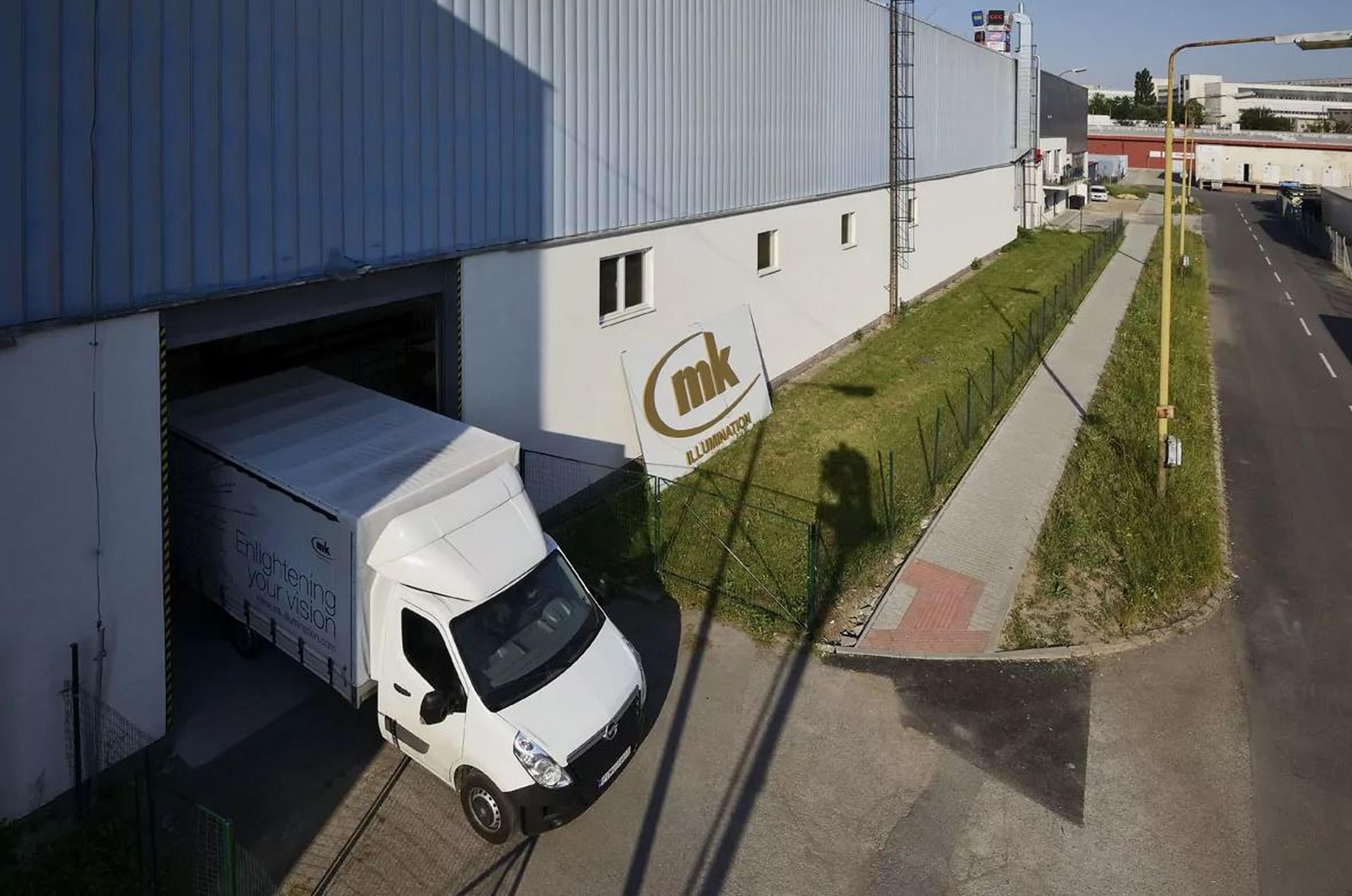 Ein Lieferwagen von MK Illumination verlässt ein Industriegebäude. Außen ist ein großes MK-Logo sichtbar.