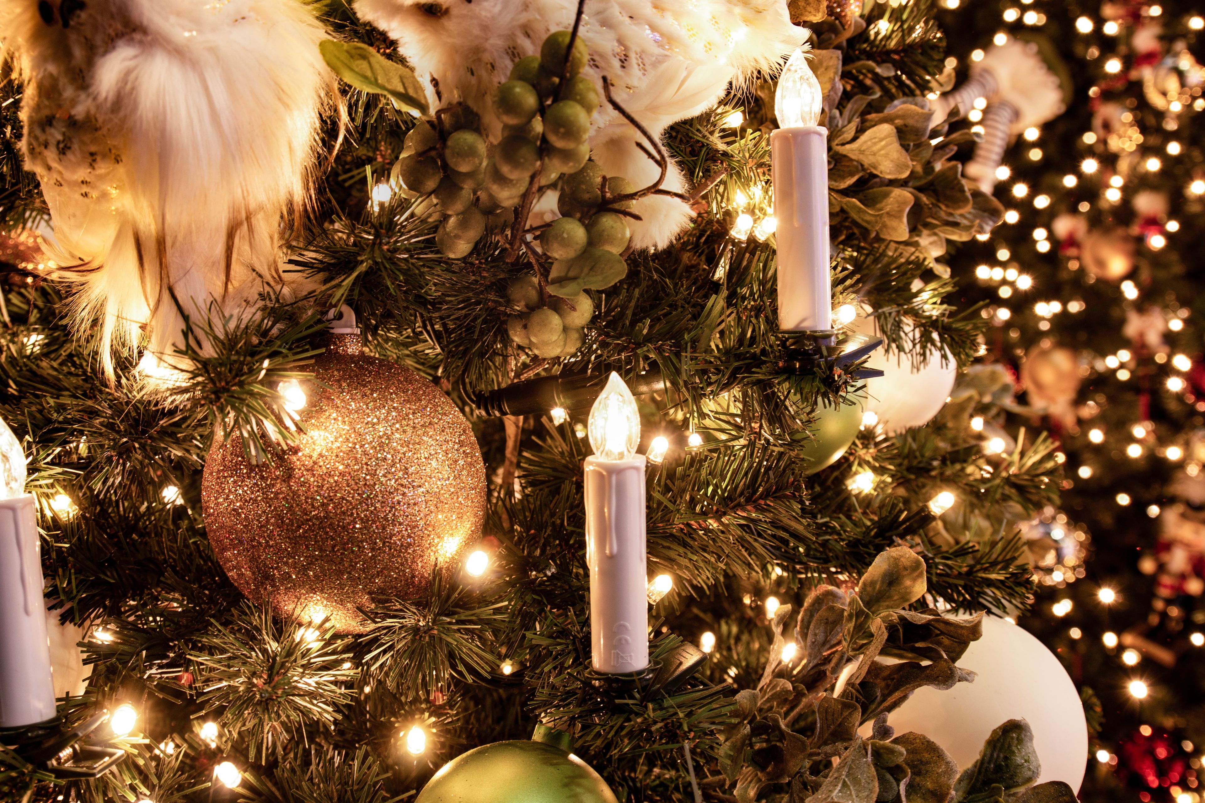Close-up of a Christmas tree with warm lights, glittery ornaments, artificial owls, and faux candles, creating a festive ambiance.
