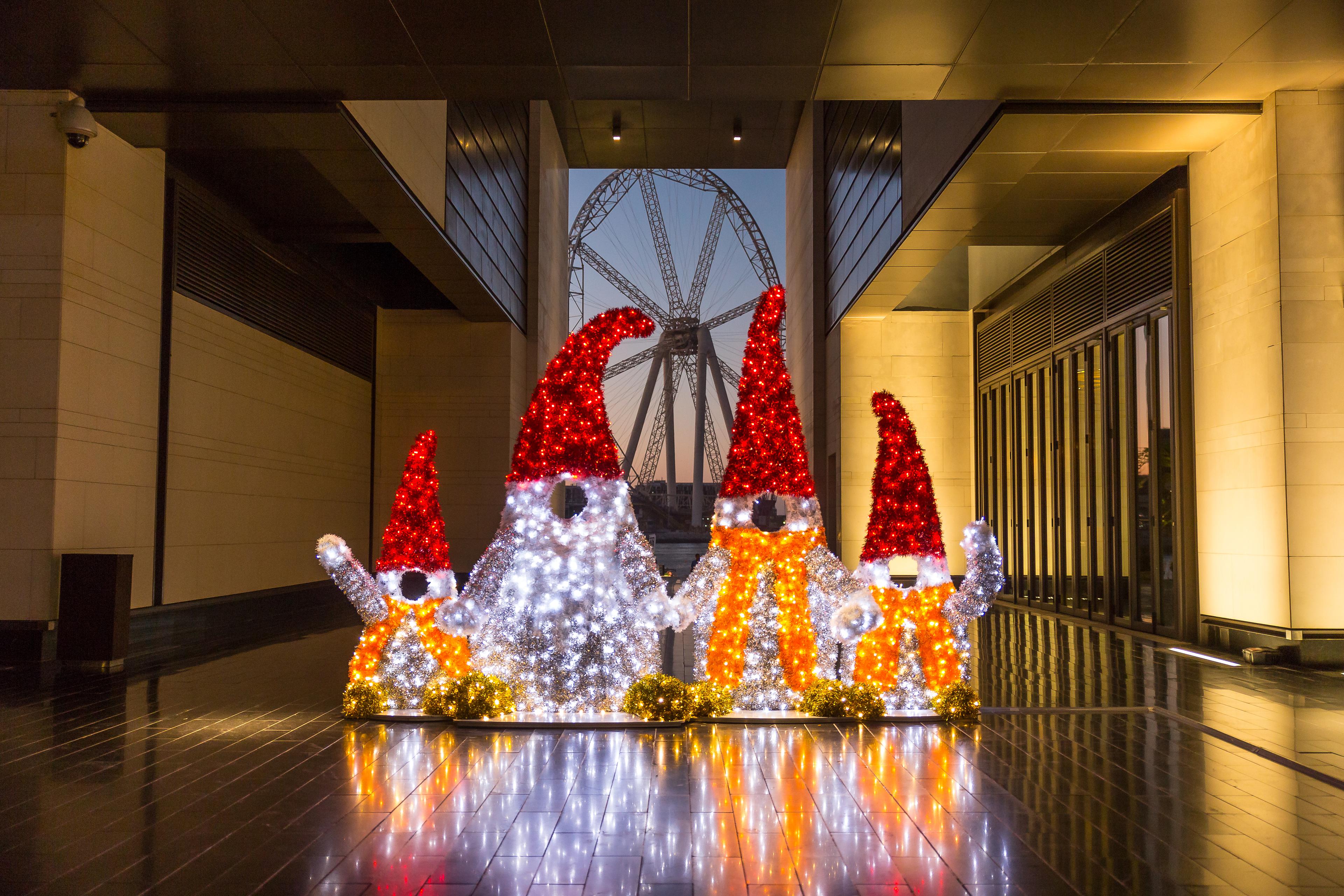 Beleuchtete Weihnachtsfiguren vor einem Riesenrad in urbanem Umfeld bei Nacht.