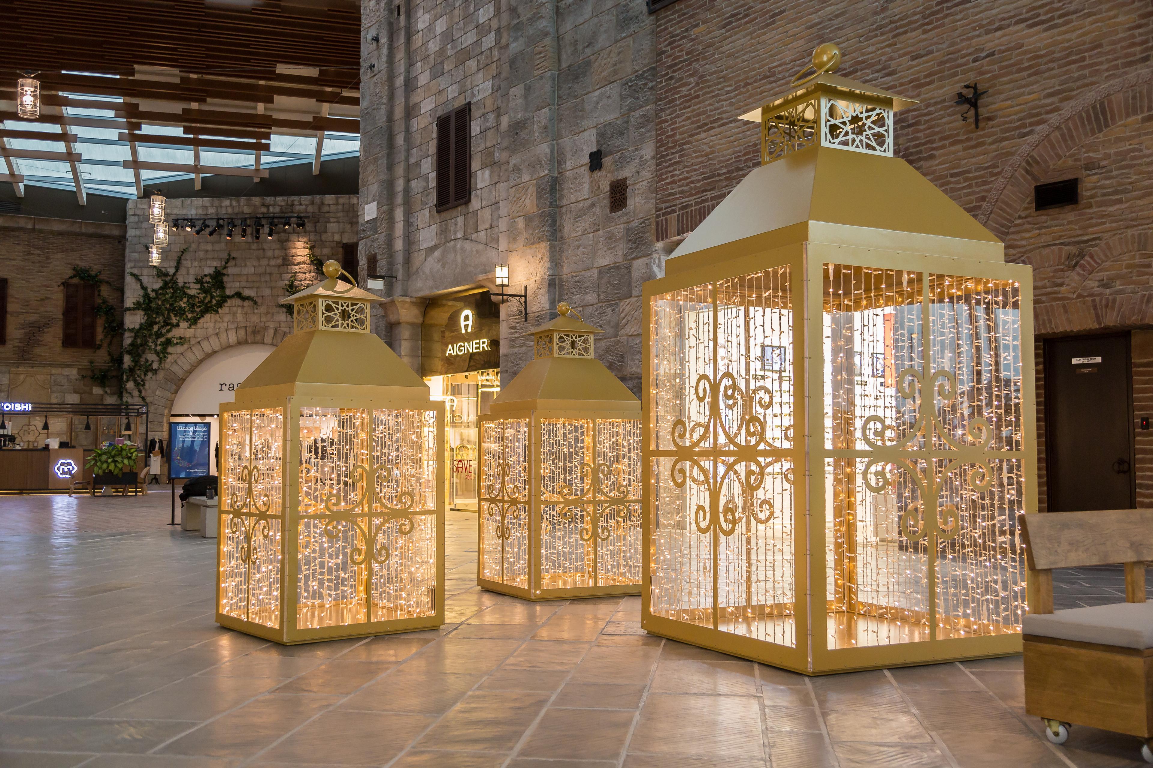 Große, goldene Laternen mit Lichterketten in einem stilvollen Einkaufszentrum aus Stein und Holz.