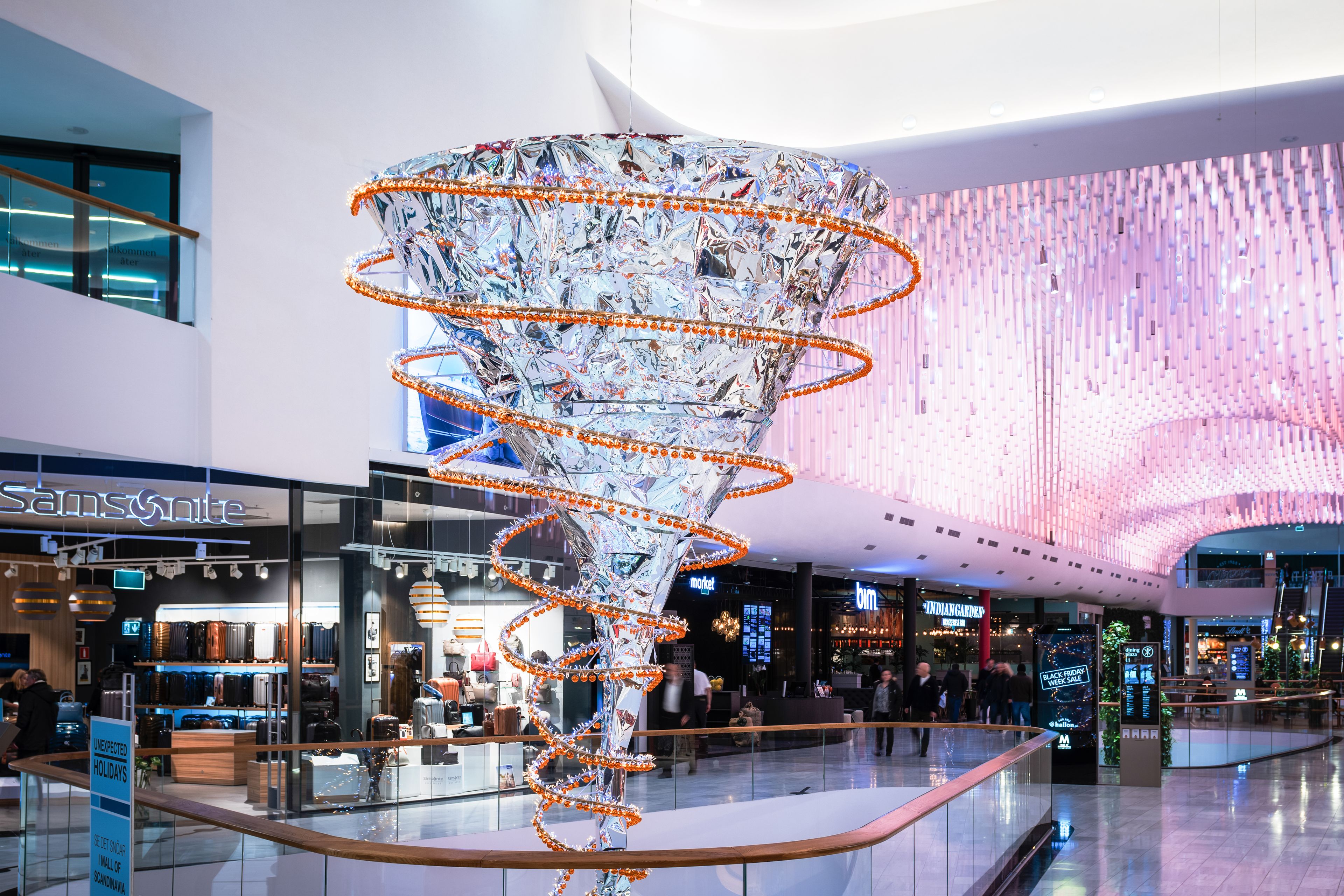 Futuristisch gestaltete Skulptur in einem hell beleuchteten Einkaufszentrum, umgeben von Geschäften und Dekorationen.