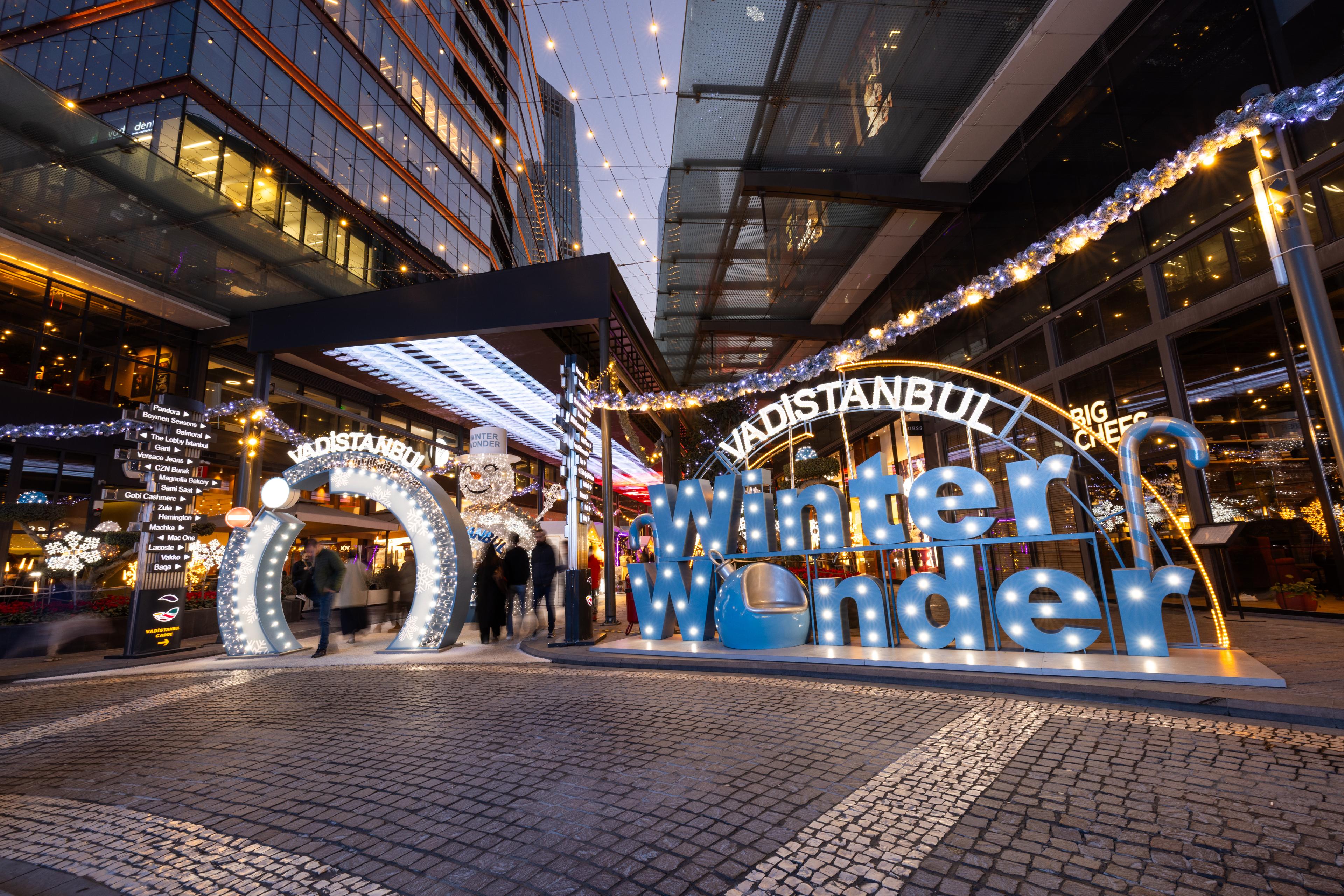 Außenansicht einer festlich beleuchteten Einkaufsstraße mit "Winter Wonder" Leuchtschrift und dekorativen Lichtelementen bei Nacht.