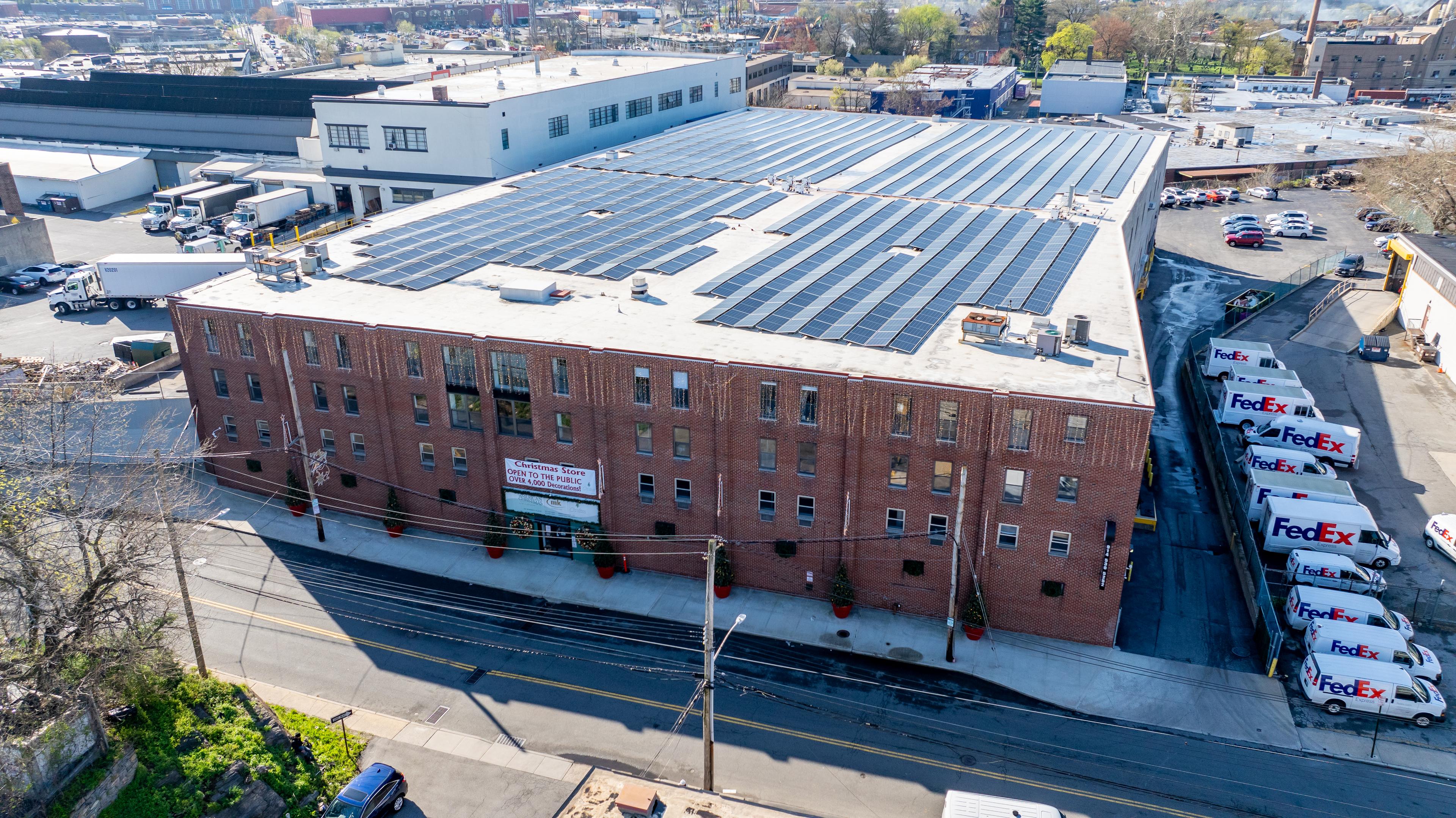 Backsteinlagerhaus mit Solarmodulen auf dem Dach und parkenden FedEx-Fahrzeugen an der Seite.