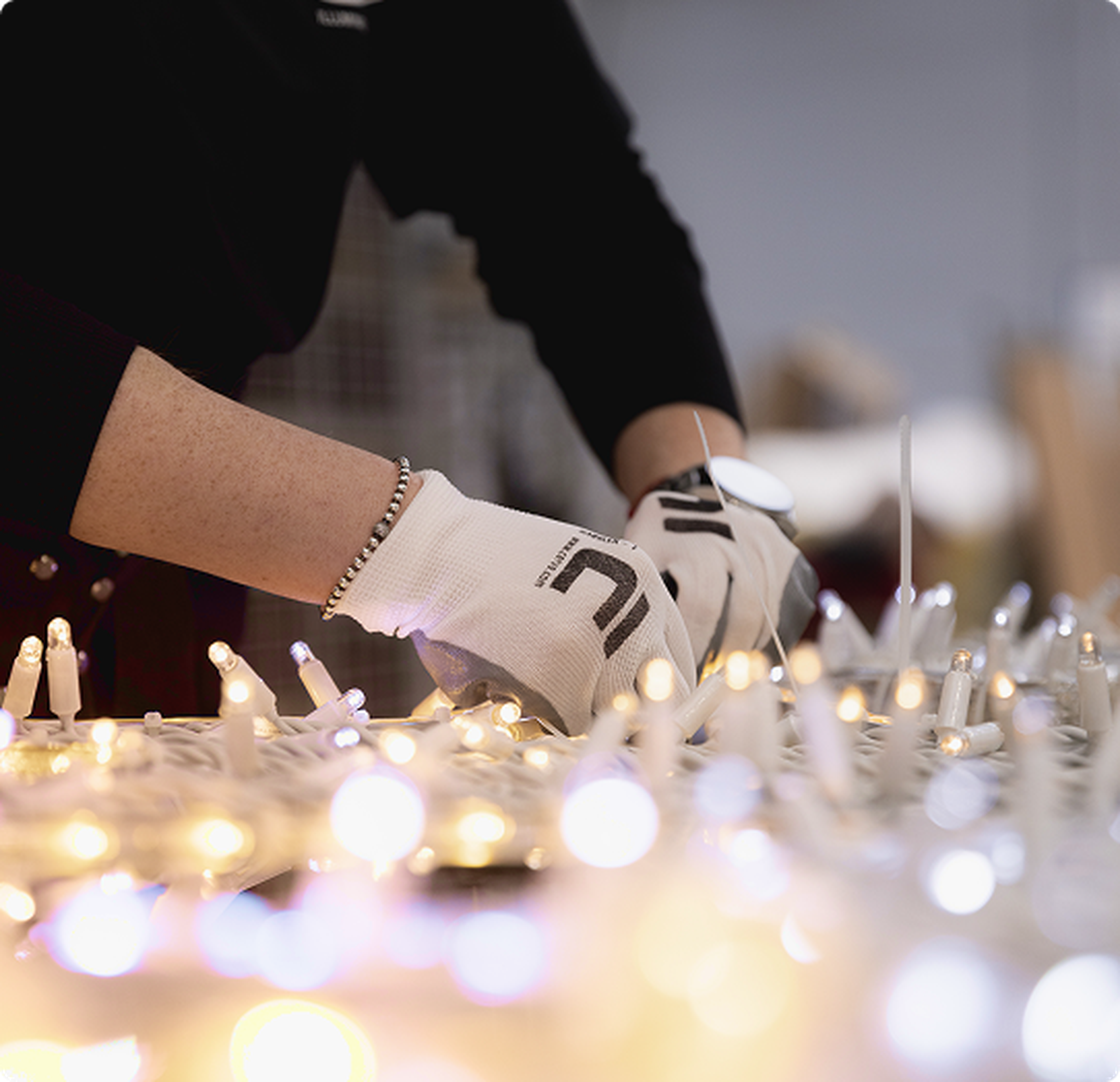 Eine Person in Handschuhen arbeitet an einer Anordnung von leuchtenden Lichtern, möglicherweise dekorative Lichterketten.