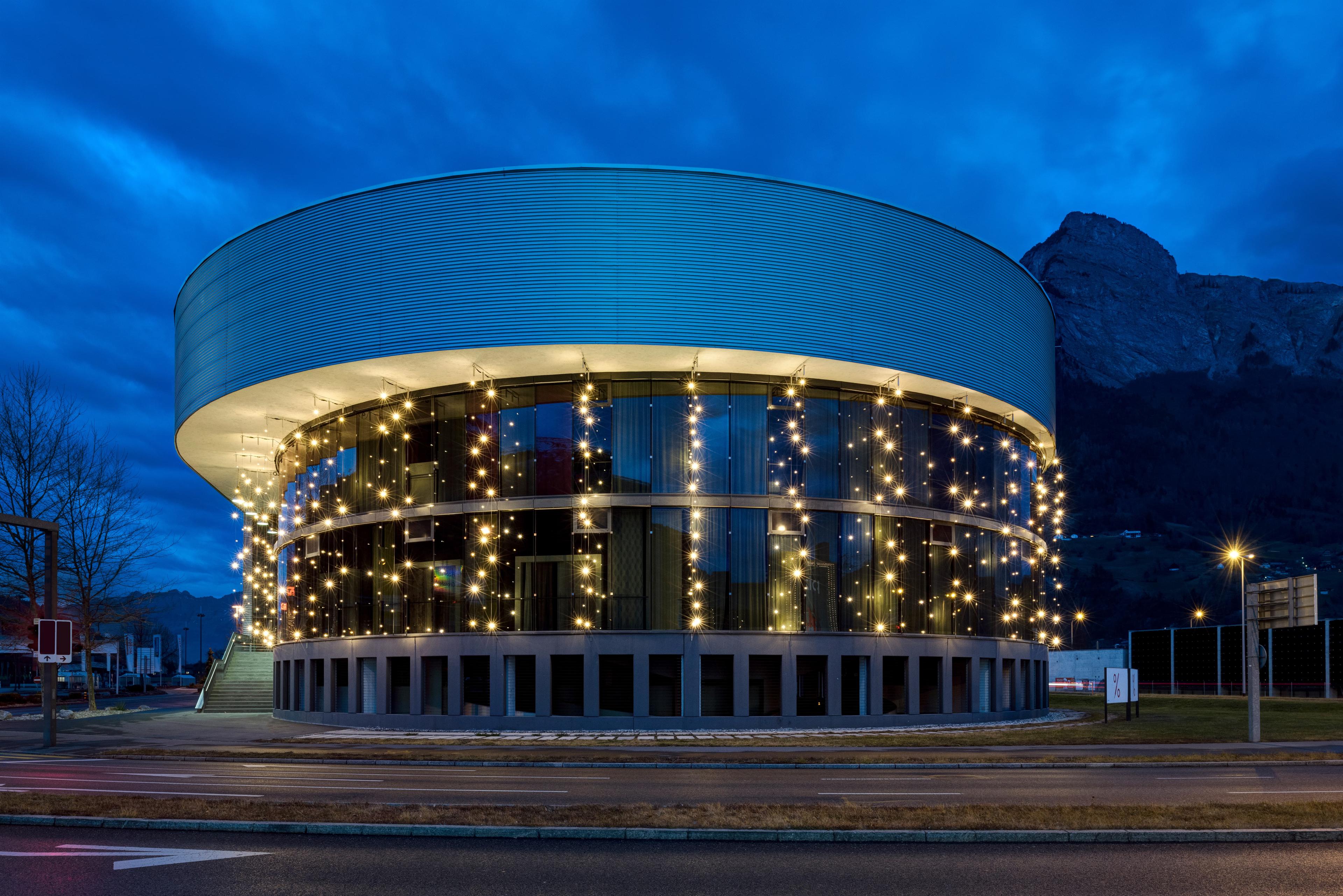 Round building adorned with twinkling lights, set against a twilight sky and mountain backdrop.