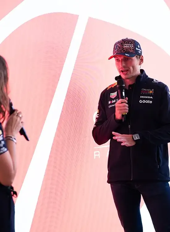 Max being interviewed, engaged in conversation against a red and white backdrop, wearing branded sports apparel.