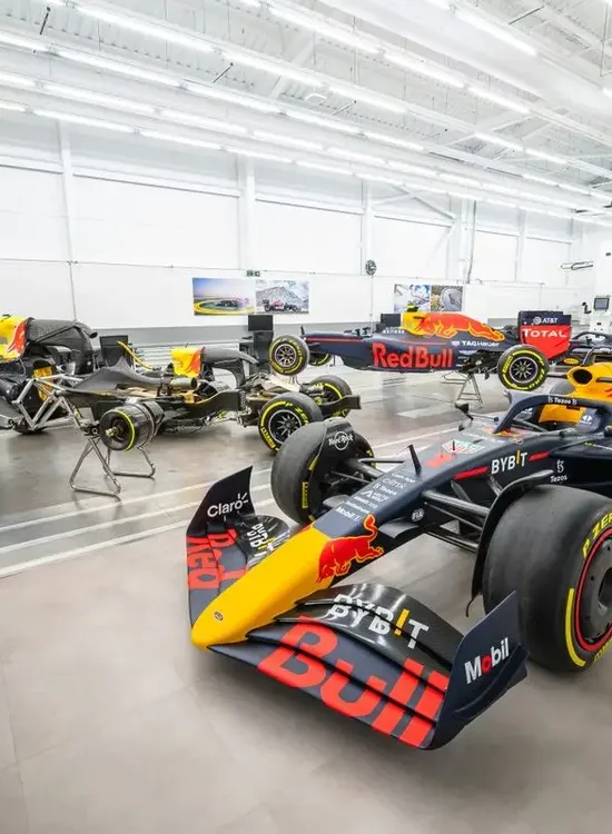 Several Red Bull Formula 1 cars are displayed in a bright, modern garage with equipment and tools.