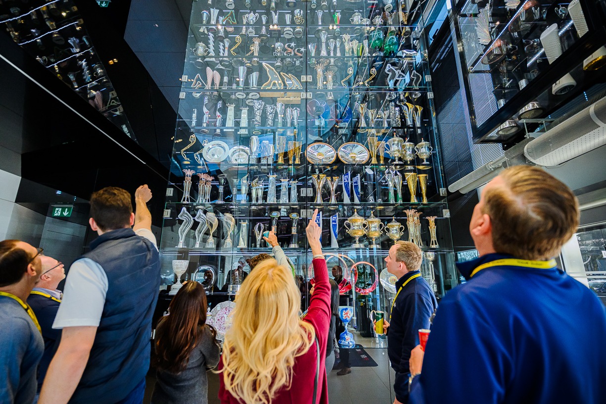 A group of people in stood in front of a tall glass display case filled with numerous trophies and awards.