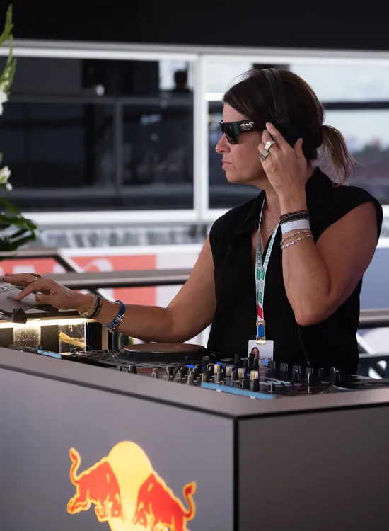 Person in sunglasses DJing at a Red Bull booth, wearing headphones and adjusting sound settings on the mixer.
