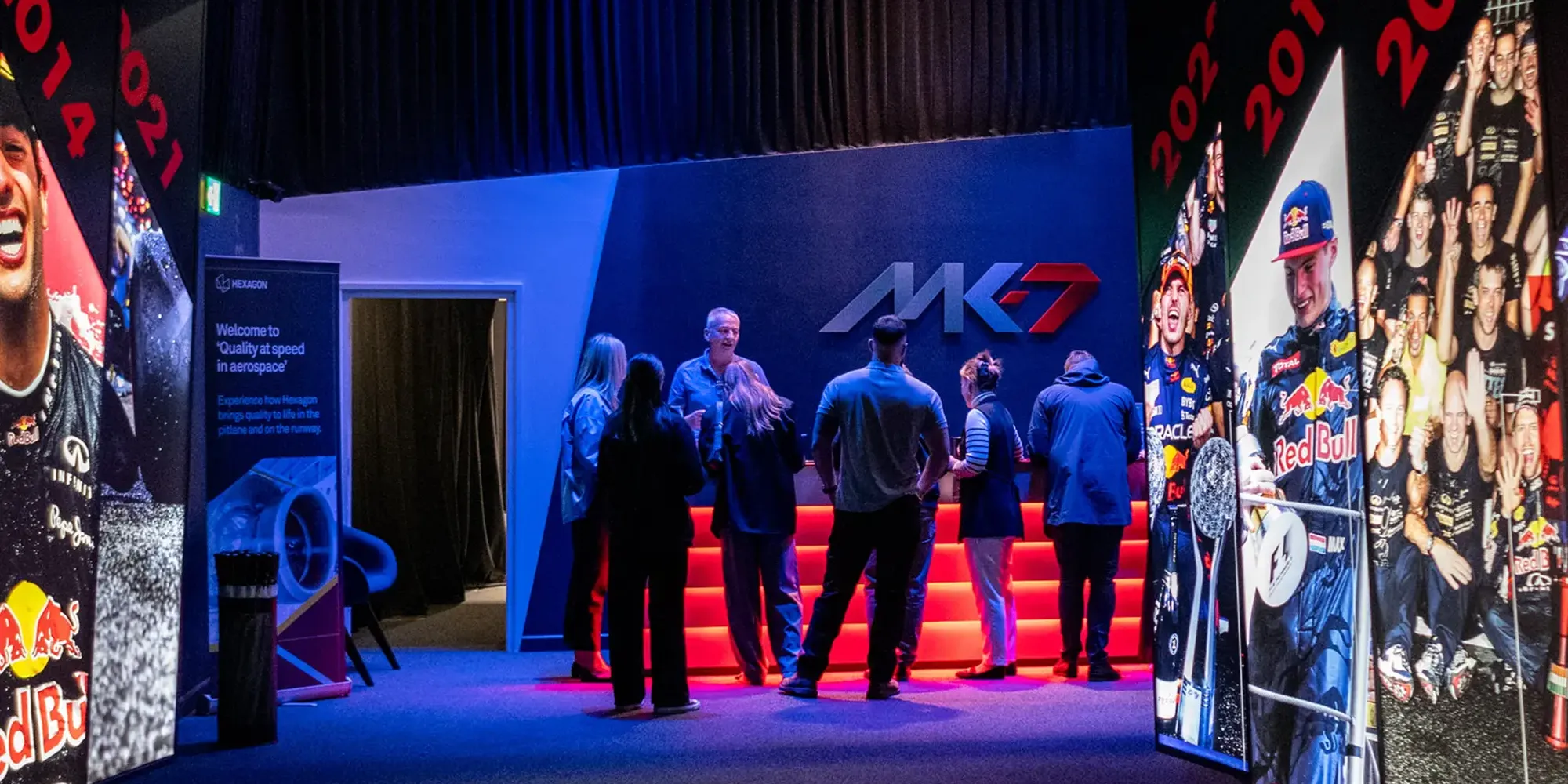 Group of people gathered at a brightly lit MK7 display, surrounded by vibrant racing-themed posters and years.