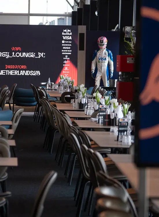 A race car driver in a suit stands beside a decorated lounge with tables set for guests.
