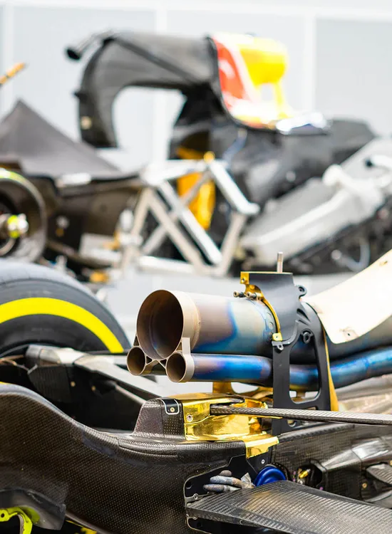 Close-up of disassembled Formula 1 car components, showcasing tires, exhausts, and chassis parts in a workshop setting.