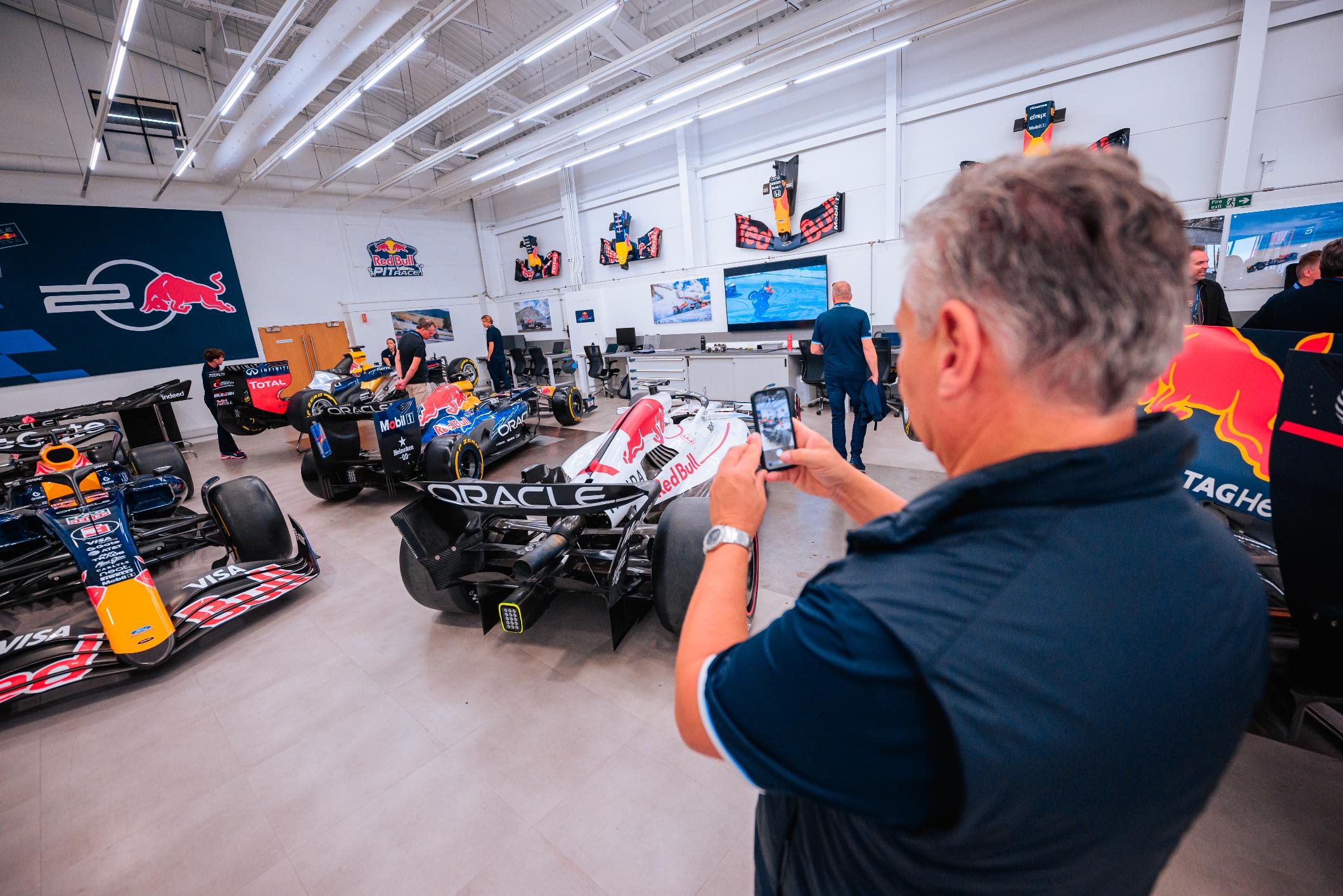 A man takes a photo of Formula 1™ cars in a showroom with Red Bull branding and racing memorabilia displayed on the walls.