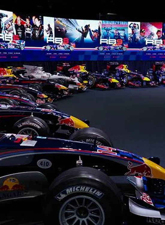A row of Red Bull Formula 1 cars displayed in our MK-7 Event Space, with a large screen above showcasing images and info related to Red Bull's racing history.