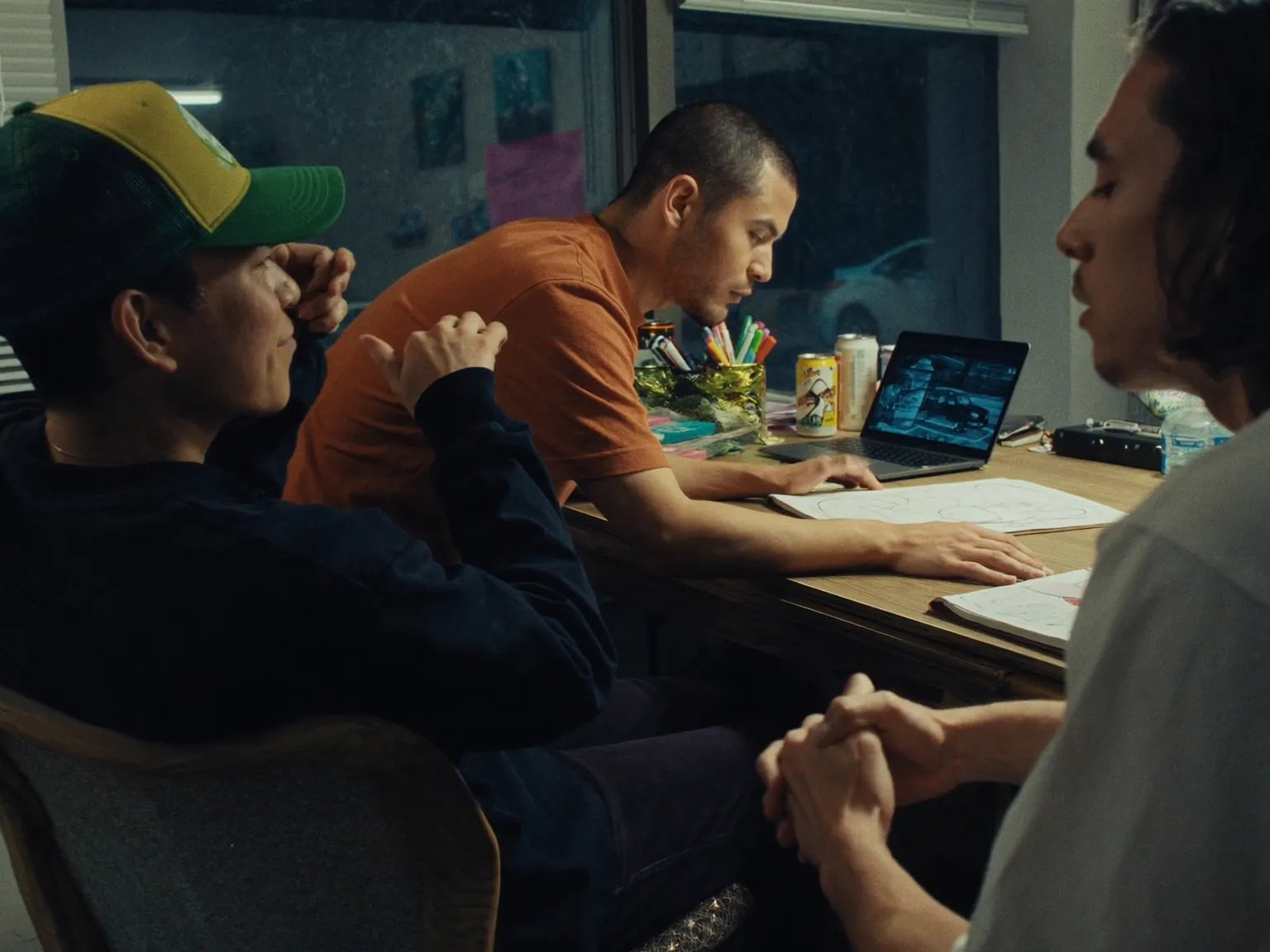 Drei Personen arbeiten an einem Tisch mit Skizzen, Unterlagen und einem Laptop.