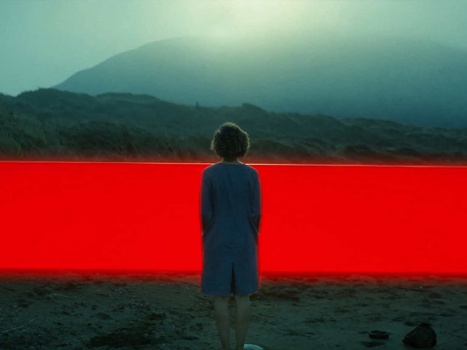 Eine Person steht in einer nebligen Berglandschaft vor einer leuchtend roten horizontalen Fläche.