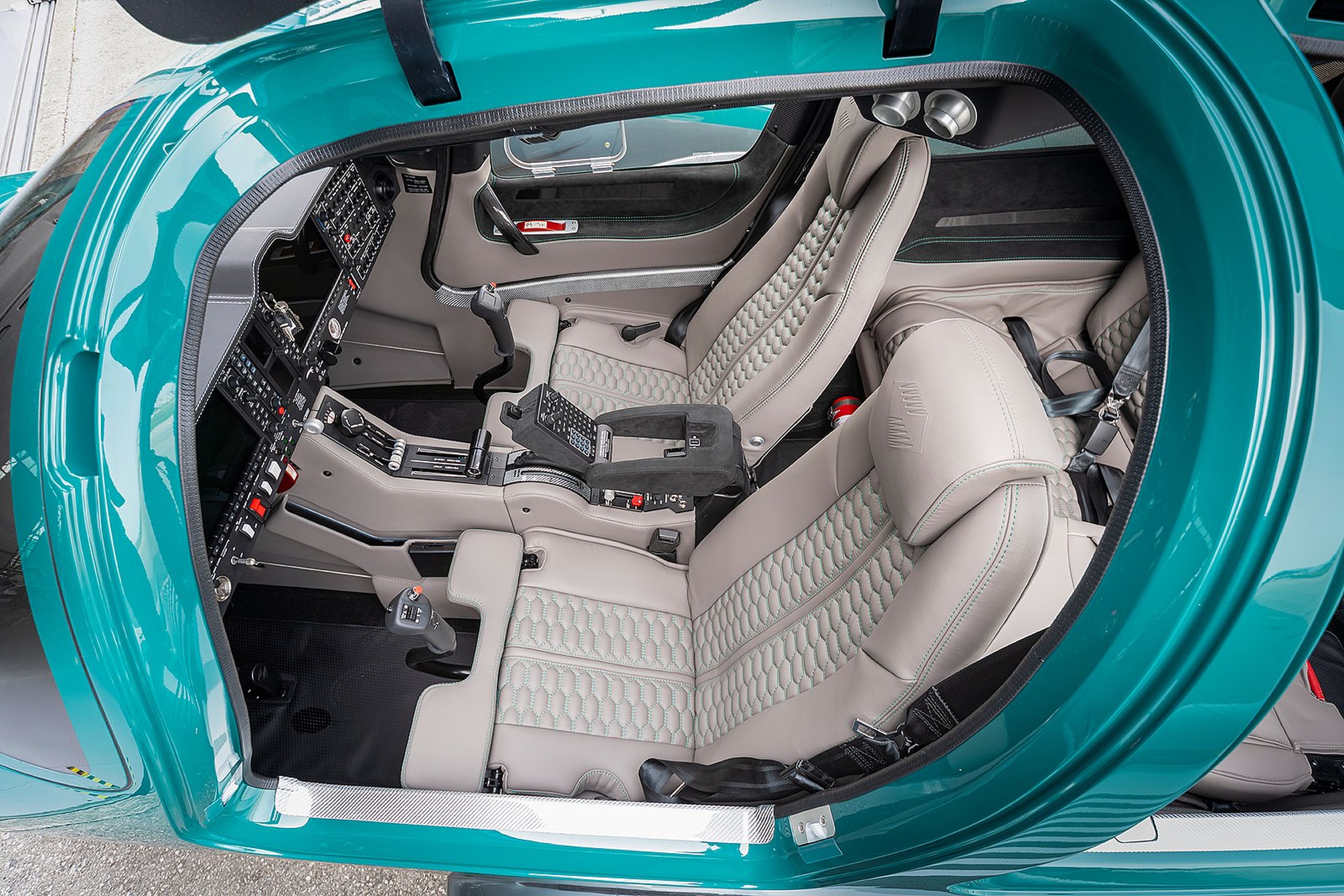 Top view of a luxurious helicopter cockpit featuring plush, quilted seats and an array of controls and instruments inside a teal frame.